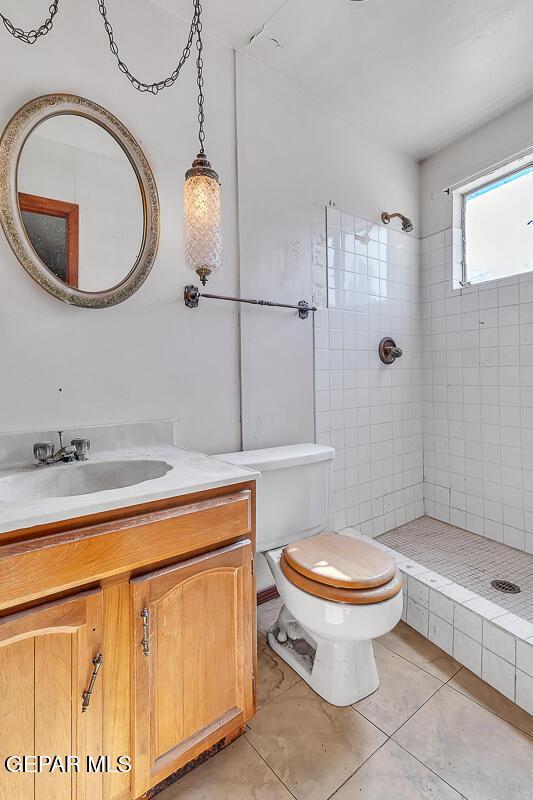 bathroom with toilet, vanity, a tile shower, and tile patterned flooring