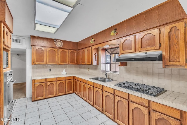 kitchen featuring appliances with stainless steel finishes, tile counters, light tile patterned floors, decorative backsplash, and sink