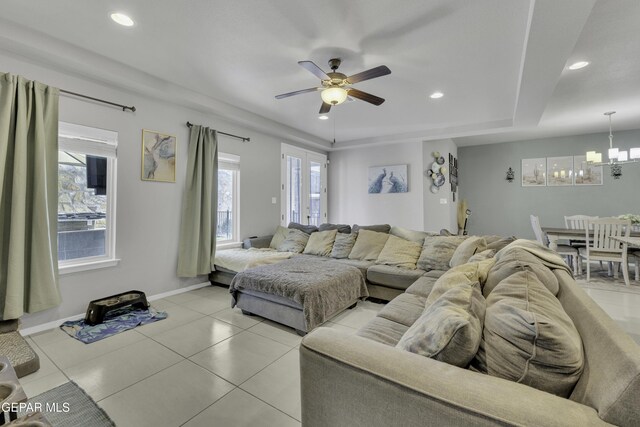 living room featuring ceiling fan with notable chandelier, light tile patterned floors, and a tray ceiling