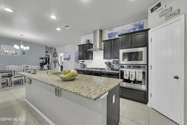 kitchen with wall chimney exhaust hood, sink, stainless steel gas stovetop, and an island with sink