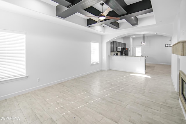 unfurnished living room featuring coffered ceiling, beamed ceiling, and ceiling fan