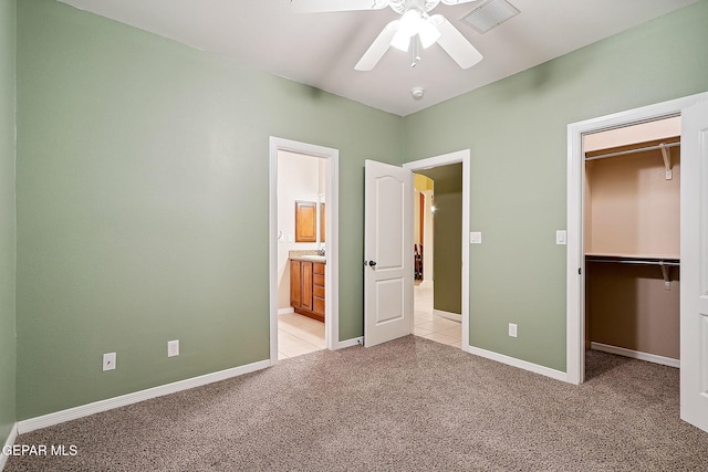 unfurnished bedroom with a spacious closet, a closet, light colored carpet, ceiling fan, and connected bathroom