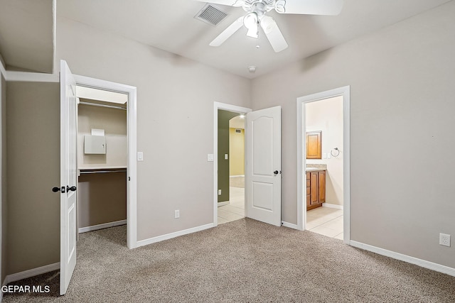 unfurnished bedroom featuring ceiling fan, light colored carpet, ensuite bath, a spacious closet, and a closet