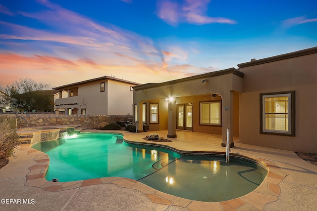 pool at dusk with an in ground hot tub and a patio area