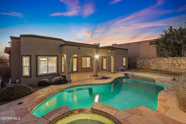 pool at dusk featuring an in ground hot tub and a patio area