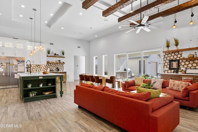 living room with ceiling fan, beam ceiling, a towering ceiling, and light wood-type flooring