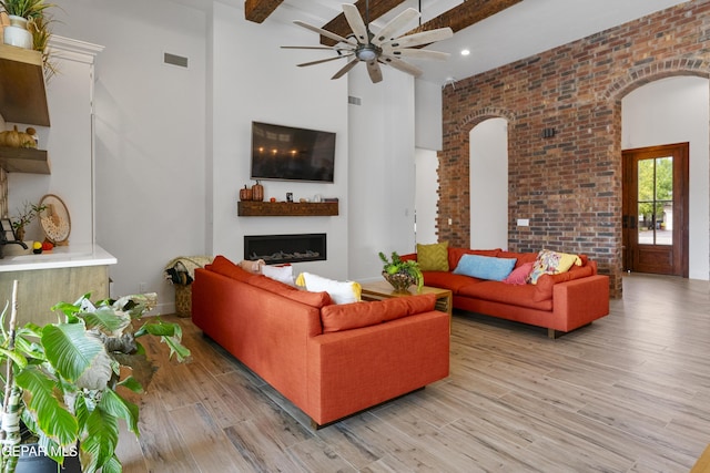 living room featuring light hardwood / wood-style floors, ceiling fan, brick wall, and beamed ceiling