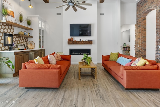 living room with ceiling fan, beamed ceiling, a towering ceiling, and light wood-type flooring