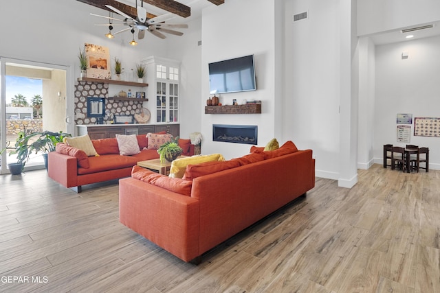 living room with a high ceiling, beam ceiling, and light wood-type flooring