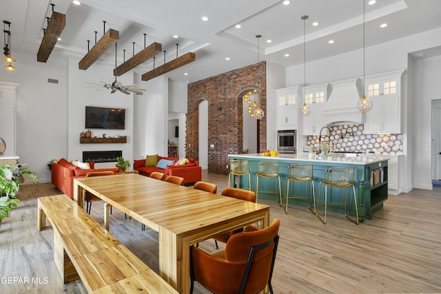 dining space with beamed ceiling, light wood-type flooring, a towering ceiling, and ceiling fan