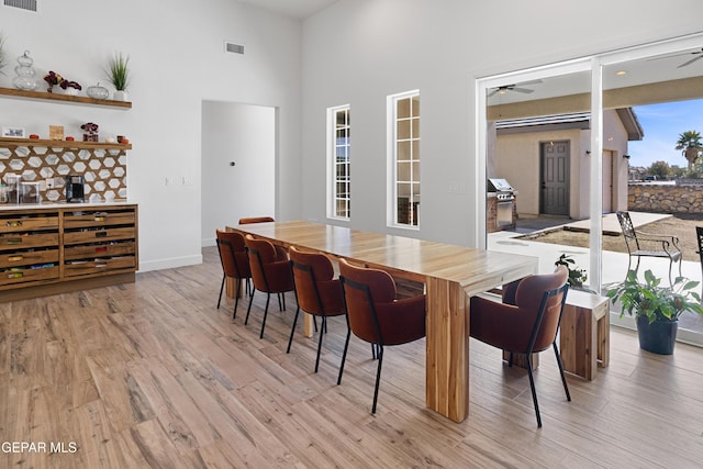 dining space featuring light hardwood / wood-style floors, ceiling fan, and a towering ceiling