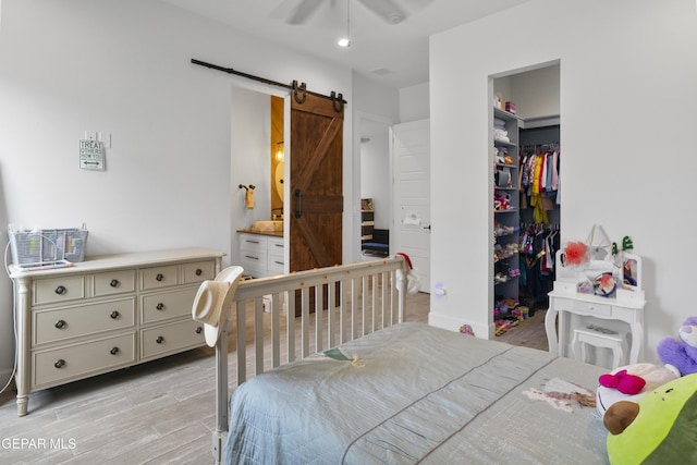 bedroom with a closet, ensuite bath, ceiling fan, and a barn door