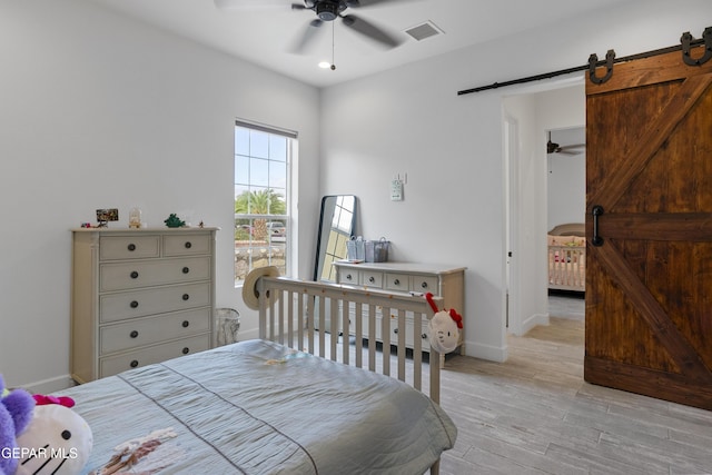 bedroom with ceiling fan, light hardwood / wood-style flooring, and a barn door