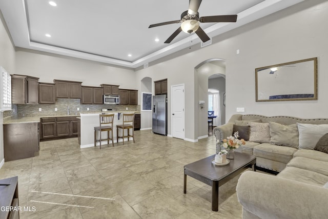 living room with ceiling fan, a high ceiling, and a tray ceiling