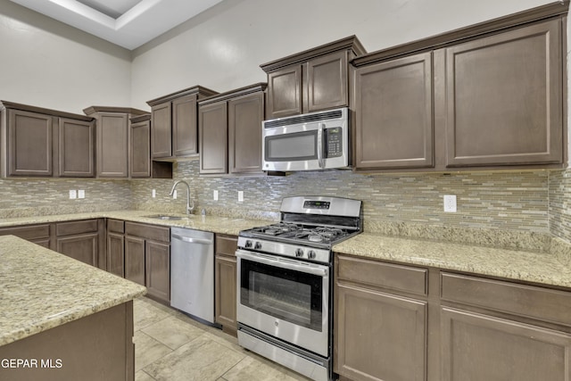 kitchen with stainless steel appliances, decorative backsplash, sink, light stone counters, and light tile patterned floors