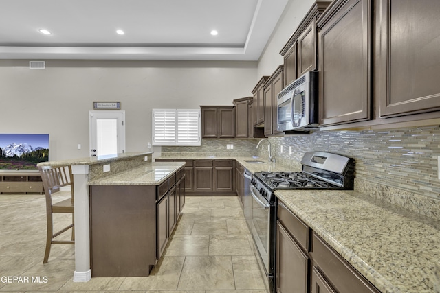 kitchen with a kitchen bar, light stone countertops, appliances with stainless steel finishes, sink, and dark brown cabinets