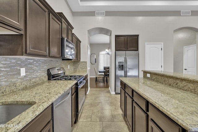 kitchen featuring appliances with stainless steel finishes, tasteful backsplash, light tile patterned floors, light stone counters, and dark brown cabinetry