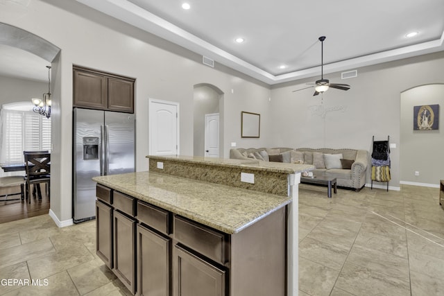 kitchen featuring light stone countertops, stainless steel fridge with ice dispenser, dark brown cabinetry, a raised ceiling, and ceiling fan with notable chandelier