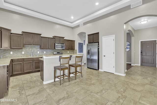 kitchen with decorative backsplash, light stone countertops, appliances with stainless steel finishes, and a center island