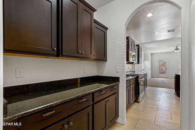 kitchen featuring ceiling fan, appliances with stainless steel finishes, dark stone counters, a textured ceiling, and dark brown cabinetry