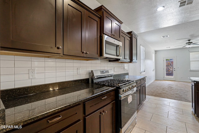 kitchen with light carpet, ceiling fan, stainless steel appliances, dark stone countertops, and dark brown cabinetry