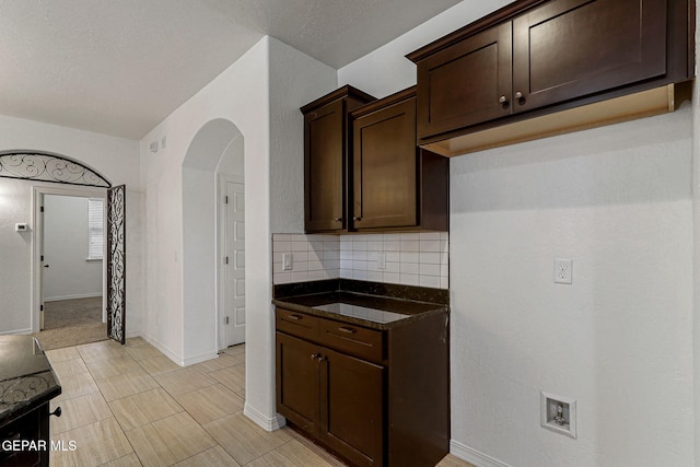 kitchen featuring dark brown cabinetry, dark stone countertops, and backsplash