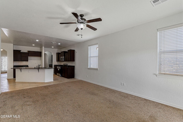 unfurnished living room with sink, ceiling fan, and light colored carpet