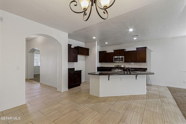 kitchen with a kitchen breakfast bar, appliances with stainless steel finishes, sink, backsplash, and an island with sink