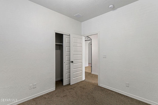 unfurnished bedroom with dark colored carpet and a closet