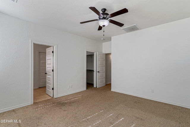 unfurnished bedroom with a walk in closet, ceiling fan, light carpet, and a closet