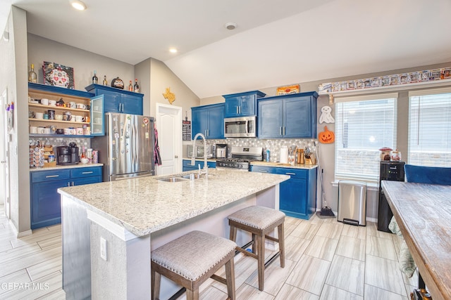 kitchen with appliances with stainless steel finishes, blue cabinets, tasteful backsplash, a kitchen breakfast bar, and a kitchen island with sink