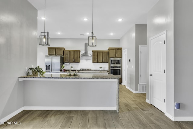 kitchen with wall chimney range hood, pendant lighting, appliances with stainless steel finishes, and kitchen peninsula