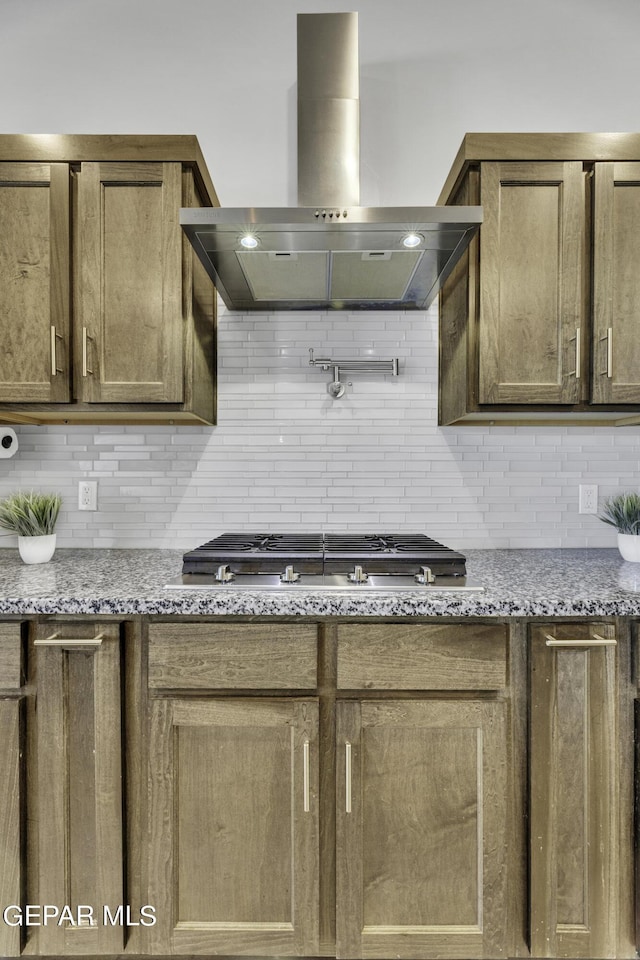 kitchen featuring light stone countertops, wall chimney range hood, stainless steel gas cooktop, and tasteful backsplash