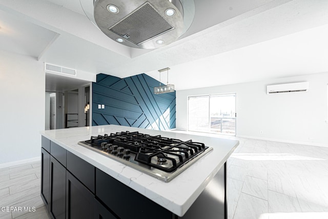 kitchen with an AC wall unit, a center island, hanging light fixtures, stainless steel gas cooktop, and light stone counters