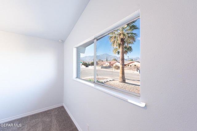 empty room featuring a mountain view, lofted ceiling, and carpet flooring