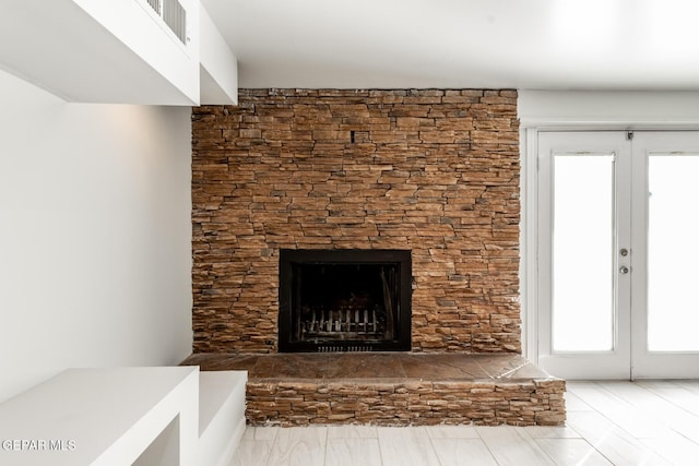 unfurnished living room with a wealth of natural light, a stone fireplace, and french doors