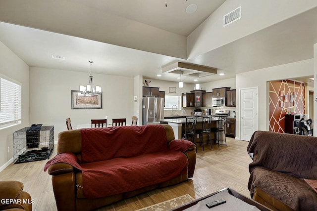 living room with sink, light wood-type flooring, a chandelier, and a healthy amount of sunlight