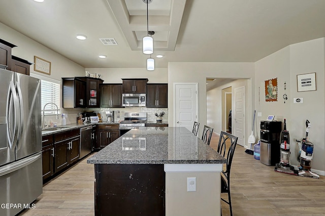 kitchen with dark brown cabinetry, appliances with stainless steel finishes, decorative light fixtures, dark stone counters, and sink