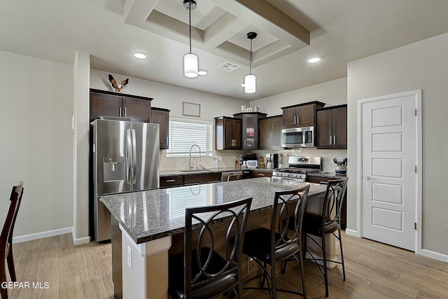 kitchen with sink, stainless steel appliances, a kitchen island, and decorative light fixtures