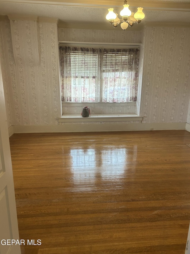 spare room with hardwood / wood-style flooring and an inviting chandelier