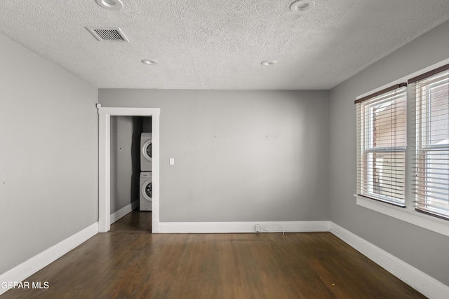 spare room with stacked washer / drying machine, dark hardwood / wood-style floors, and a textured ceiling