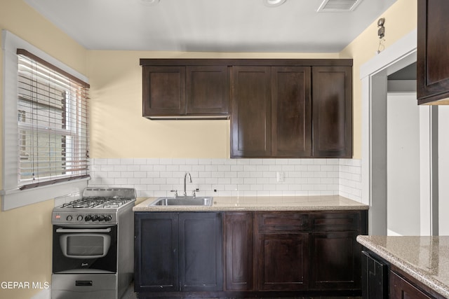 kitchen featuring sink, dark brown cabinetry, light stone counters, tasteful backsplash, and gas stove