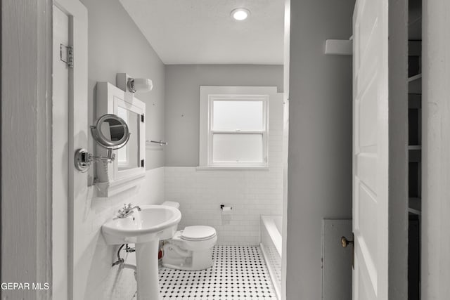 bathroom featuring tile walls, a bathtub, toilet, tile patterned floors, and a textured ceiling