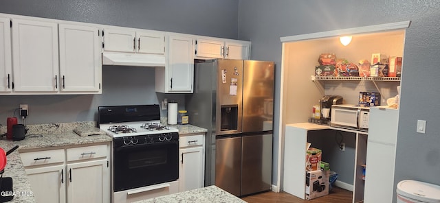 kitchen featuring gas range, light stone countertops, stainless steel fridge with ice dispenser, and white cabinets