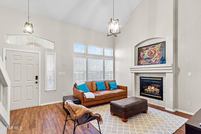 living room featuring high vaulted ceiling, hardwood / wood-style floors, a notable chandelier, and a tiled fireplace