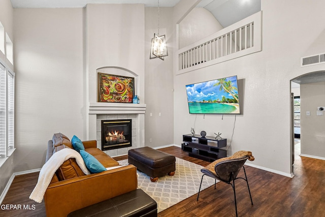 living room with dark wood-type flooring, an inviting chandelier, a towering ceiling, and a fireplace