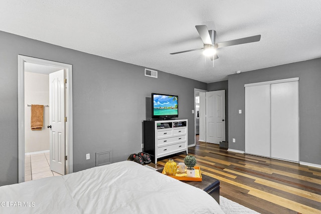 bedroom featuring a textured ceiling, ensuite bath, a closet, dark hardwood / wood-style flooring, and ceiling fan