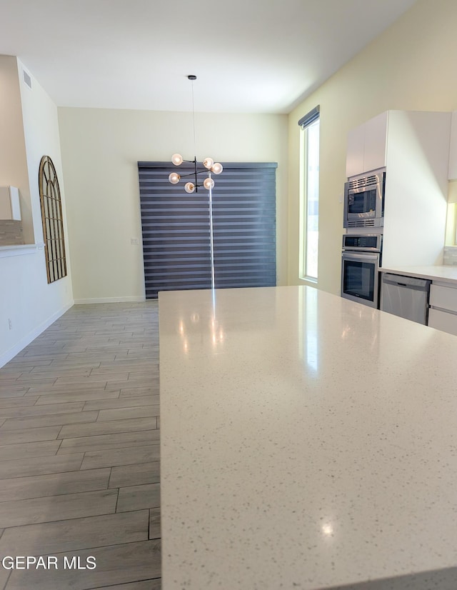 kitchen featuring stainless steel appliances, hanging light fixtures, white cabinets, and light wood-type flooring