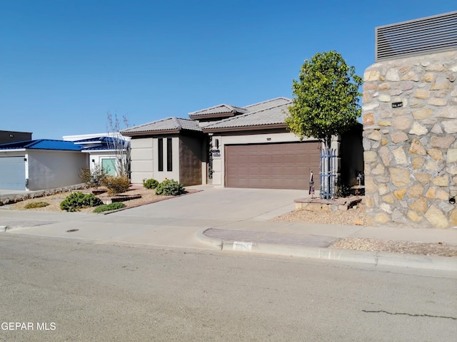 prairie-style house with a tile roof, an attached garage, stucco siding, and concrete driveway