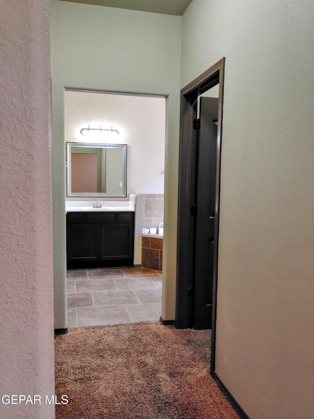corridor featuring a textured wall, a sink, and light tile patterned floors